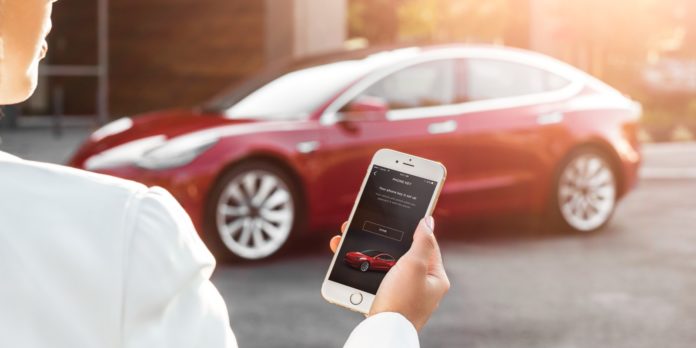 Model 3 in background with woman holding phone showing Tesla mobile app