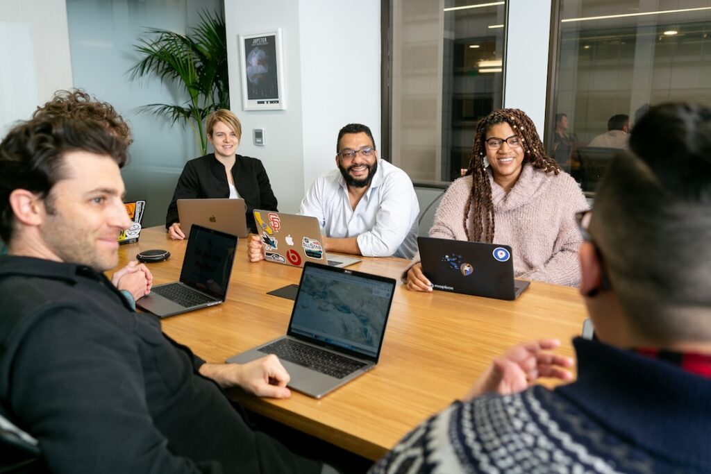 A team at a conference table with laptops discussing resource management tools.